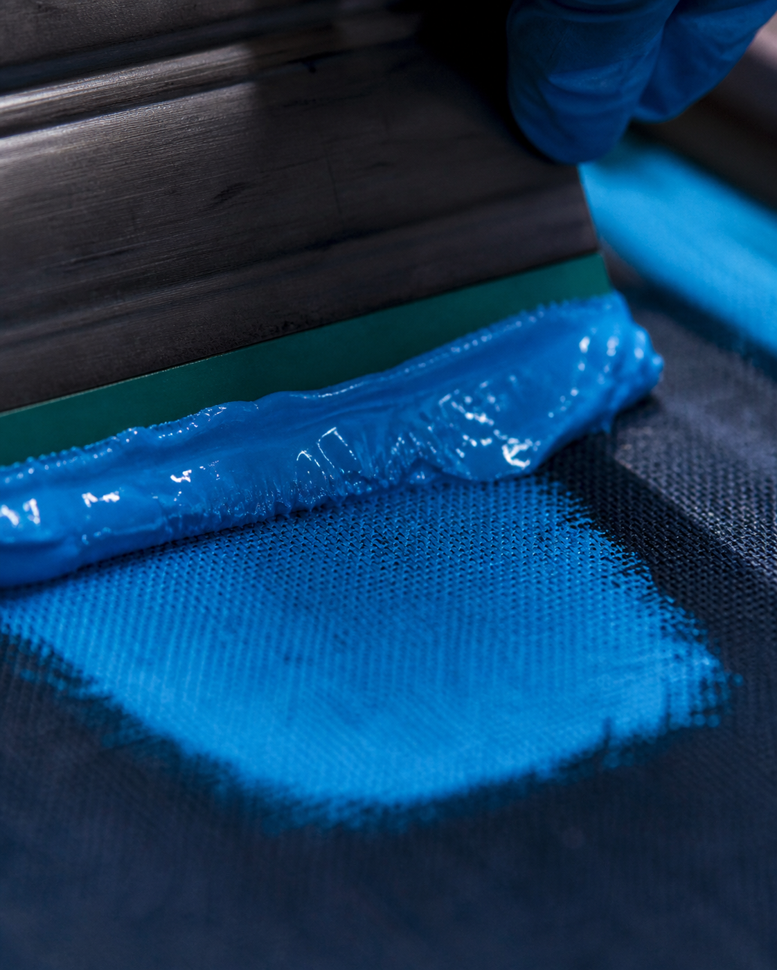 Screen printer pulling blue ink across a shirt
